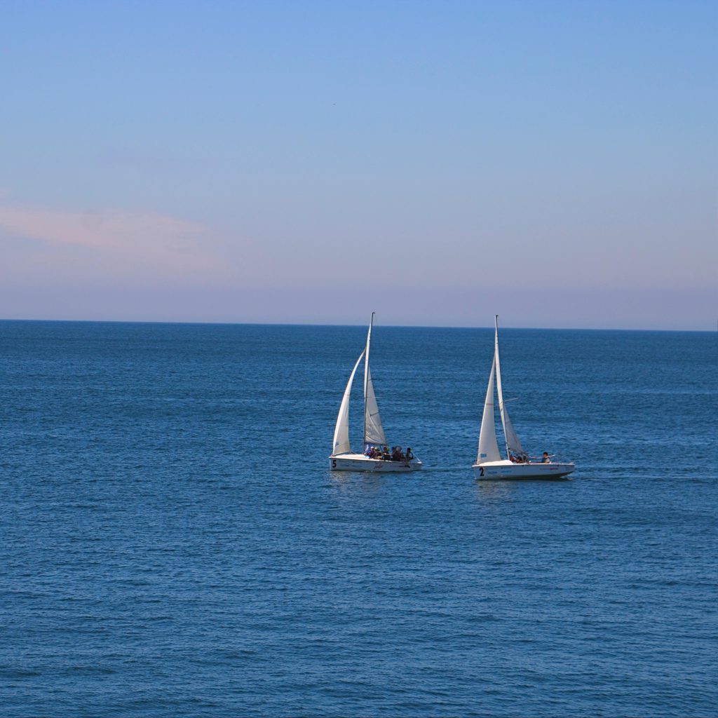 Two sailboats peacefully sail on a calm ocean under a clear blue sky.