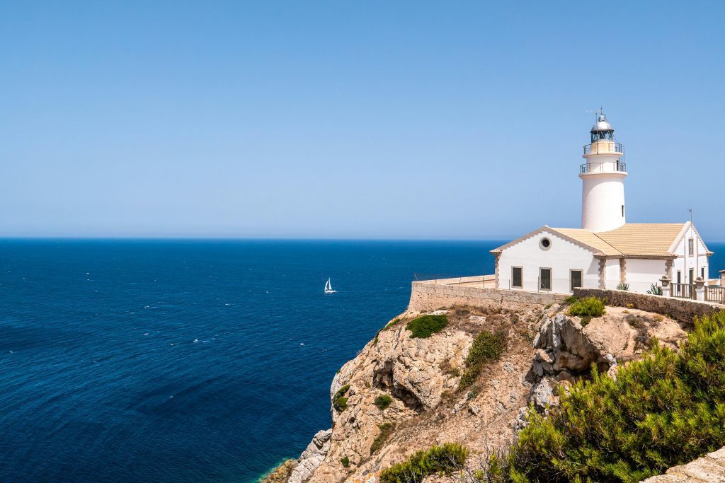 Breathtaking view of a lighthouse perched on Mallorca's rugged coastline overlooking the blue Mediterranean Sea.