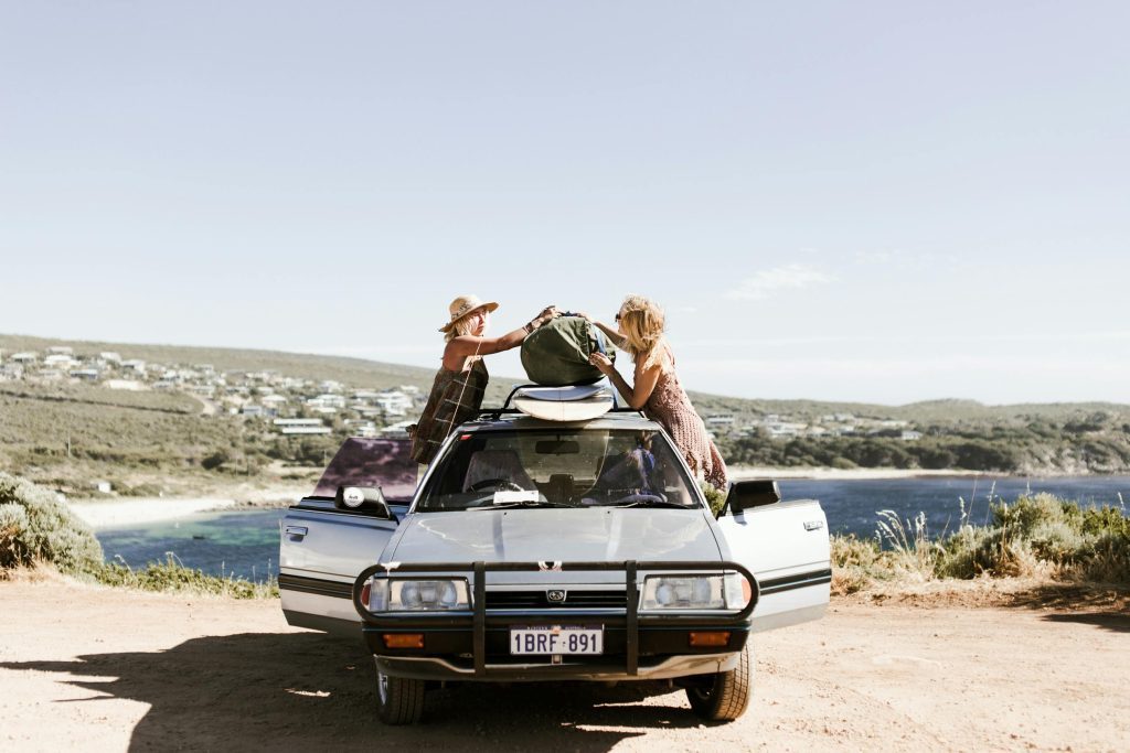 Two women packing a car near a beautiful coastal landscape, under clear skies. Mallorca Yacht