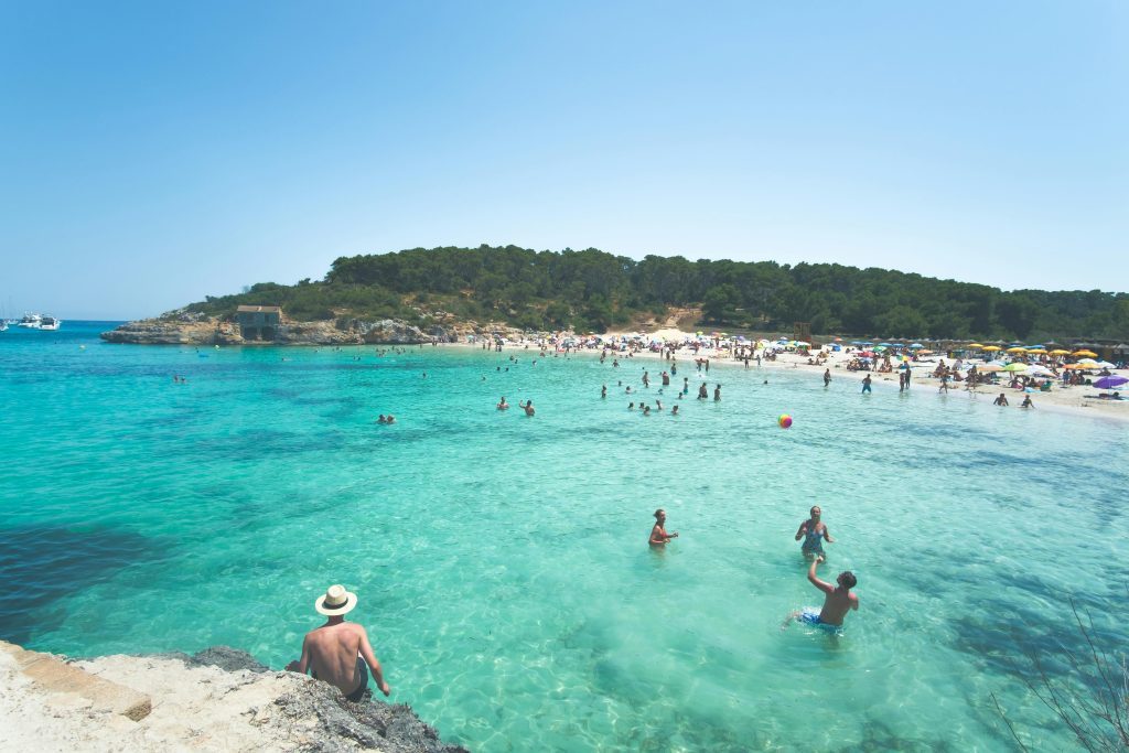 People enjoying a lively summer day at a tropical beach in Mallorca with turquoise water.