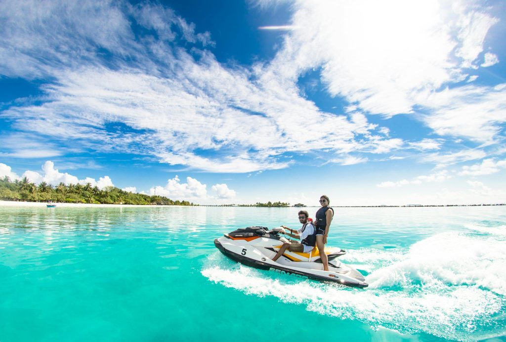 Couple enjoying a thrilling jet ski ride on crystal clear waters under a bright sky in Maldives.