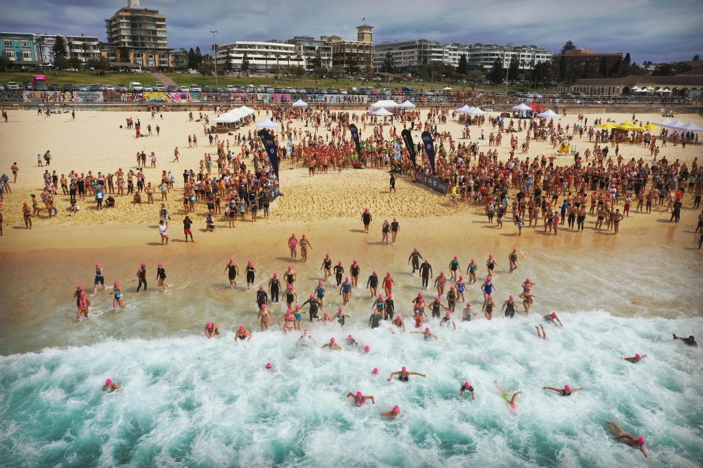 A vibrant beach swim event with swimmers diving into the ocean under a sunny sky.