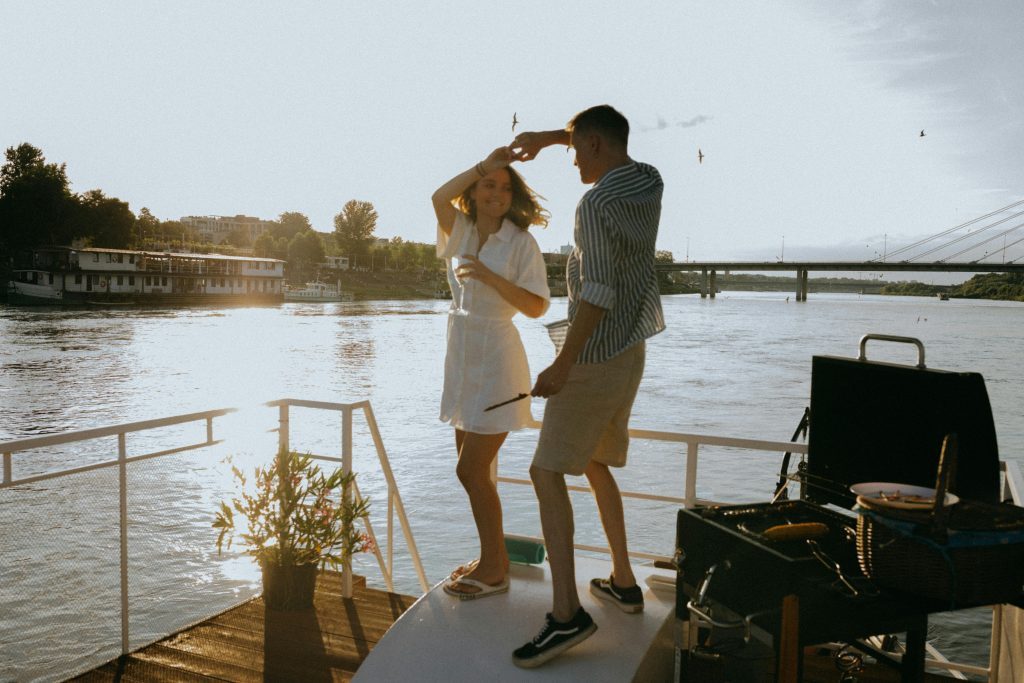 A couple enjoys a romantic dance on a yacht during a vibrant sunset with scenic river views.